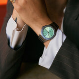 Person wearing a watch with a pistachio green dial and silver case, dressed in a suit.
